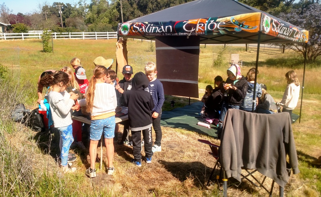 The kids gathering around the display table to see and touch the many items.